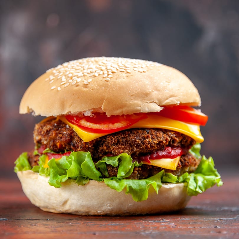 A double hot chicken burger with cheese, tomato, and lettuce on a sesame seed bun.